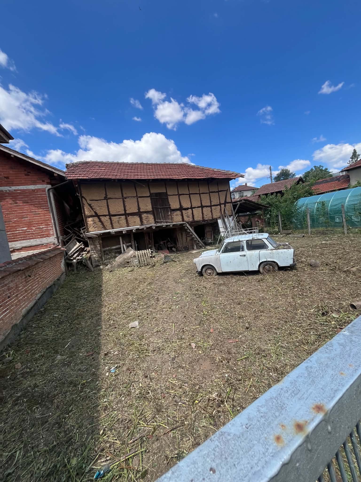 Стара стопанска постройка и изоставен автомобил в двор преди разчистване